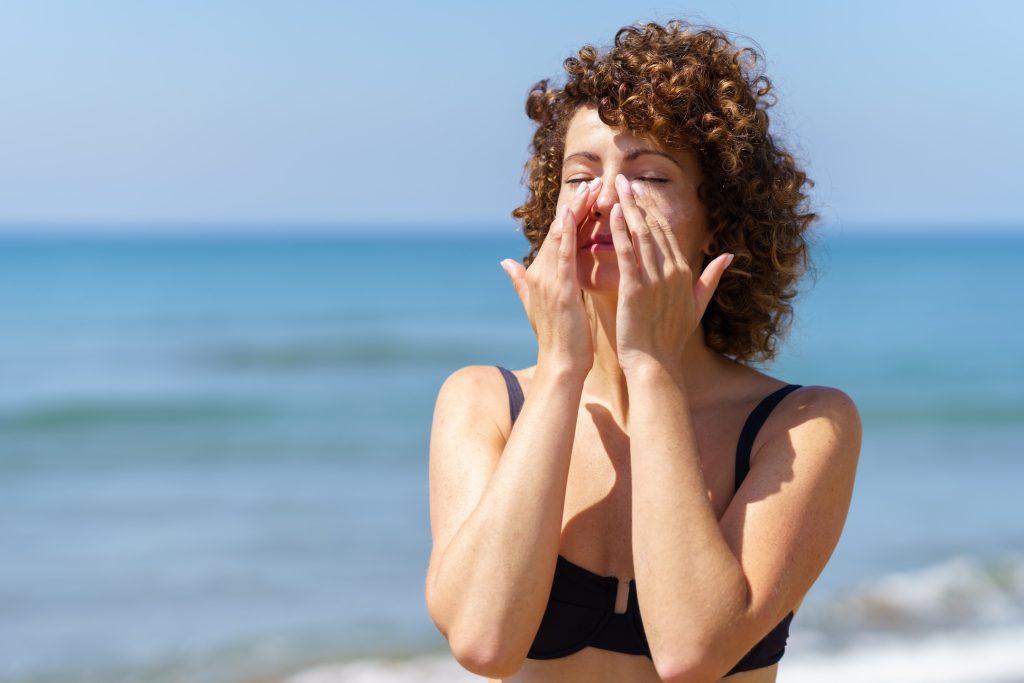 young woman in bikini applying best tinted sunscreen on face