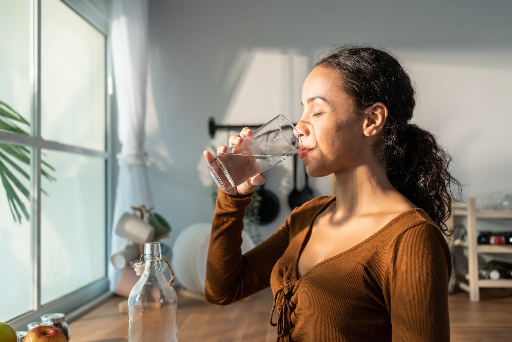 young woman drinks water to hydrate her dehydrated skin