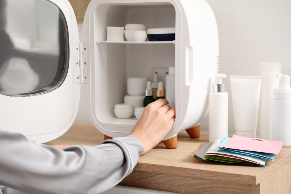 woman's hand reaching into a small white fridge for skincare filled with various beauty items