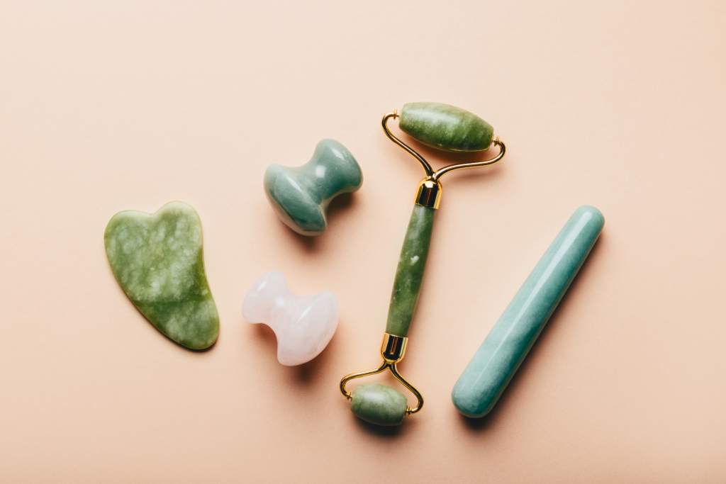 green and pink gua sha stones and a green jade roller on a neutral background can be kept chilled like other fridge skincare