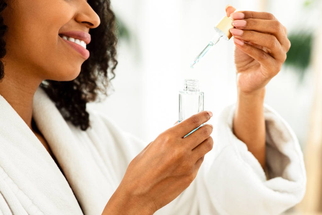 young woman wearing a white robe holding a bottle of clear serum deciding what skincare to keep in fridge