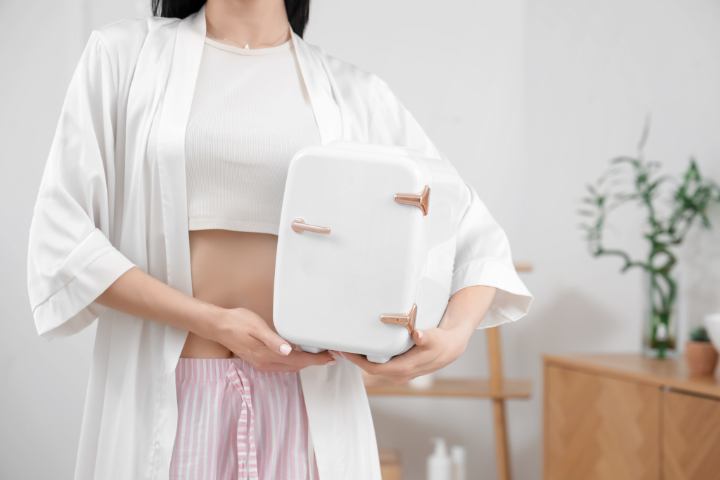 young woman holding a white skincare fridge pondering what to put in mini fridge skincare and beauty items